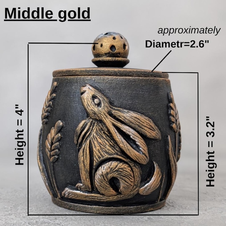 Puede incluir: Un tarro decorativo negro con un dise&ntilde;o de conejo dorado y tapa. El tarro mide aproximadamente 10 cm de alto y 6,6 cm de di&aacute;metro. El tarro tiene una altura de 8,1 cm. La tapa tiene un dise&ntilde;o perforado. El texto "Middle gold" es visible.