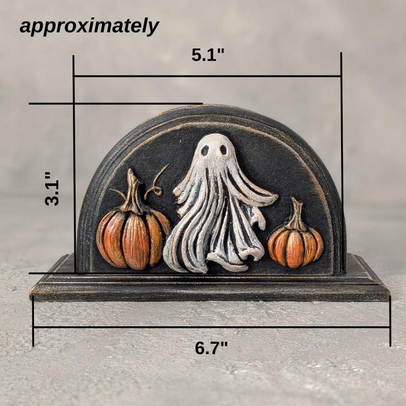 May include: A semi-circular black decorative stand featuring a raised white ghost figure flanked by two orange pumpkins. The piece measures approximately 13 cm in height, 7.9 cm in depth, and 17 cm in width as indicated by the text.