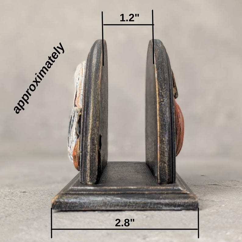 May include: A dark, distressed-finish wooden napkin holder with two upright panels and a flat base. The interior width measures 1.2 inches, and the total base width measures 2.8 inches, as indicated by the text and lines on the image.