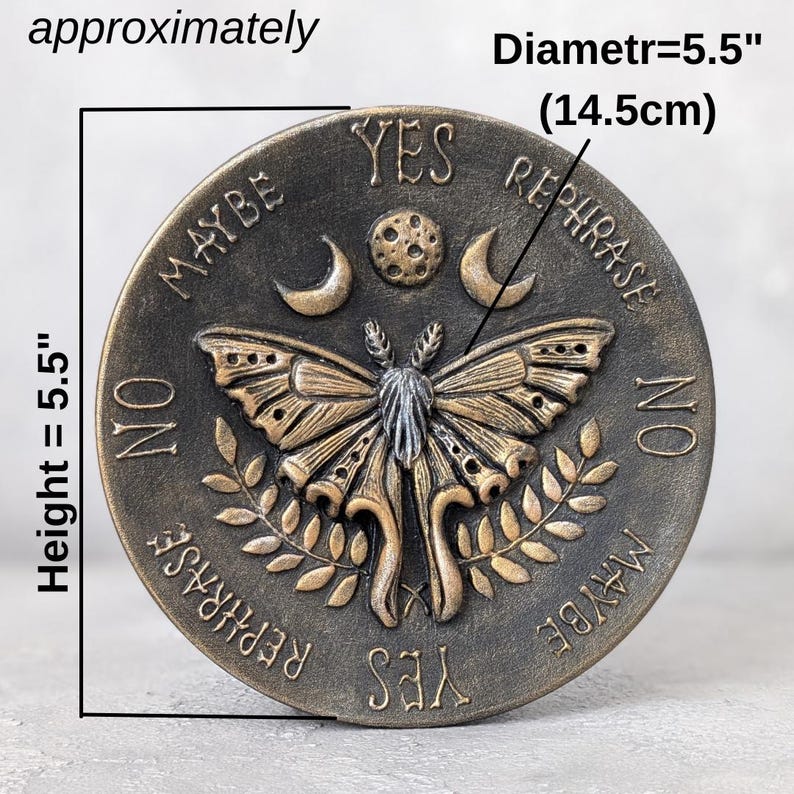 May include: A circular bronze-toned plaque featuring a central moth, moon, and sun design. The text reads YES, NO, MAYBE, and REPHRASE. It measures 5.5 inches in height and 5.5 inches in diameter. The surface has a weathered, textured finish.