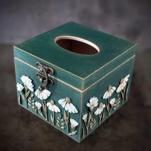 May include: A set of three ceramic mugs with a speckled, cream-colored glaze. Each mug features a different hand-painted floral design in shades of blue, green, and yellow. The mugs have a simple, rounded shape and a comfortable handle.
