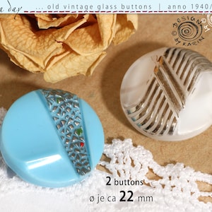 May include: Two round glass buttons with a diameter of 22 mm. One button is light blue with a textured silver-coloured diagonal stripe, and the other is white with a raised silver-coloured striped pattern. Text reads: rosa day, old vintage glass buttons, anno 1940/50/60, design by karin, 2 buttons, ø je ca 22 mm.