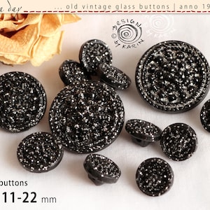 May include: A selection of 12 vintage black glass buttons with silver glitter detailing. The buttons range in size from 11 to 22 mm. The image includes text that says "old vintage glass buttons anno 1950/60" and "design by Karin".