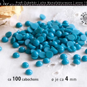 Puede incluir: Un montón de aproximadamente 100 cabujones turquesa, cada uno mide aproximadamente 4 mm de diámetro. Los cabujones están dispersos sobre una superficie blanca.
