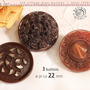 May include: Three round vintage glass buttons with a diameter of 22 mm. One button is dark brown with silver-colored leaf-like accents, one is a dark metallic brown with a swirling textured pattern, and one is a translucent reddish-brown with a floral rim.