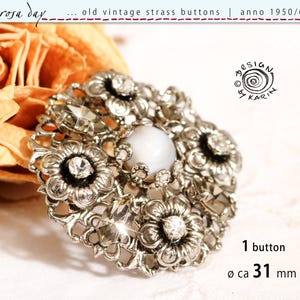 Op de afbeelding: Een ronde vintage knoop met een zilverkleurige metalen filigraan basis, voorzien van een centrale witte cabochon omringd door bloemmotieven en heldere strass-kristallen. De knoop heeft een diameter van ca. 31 mm, zoals aangegeven in de tekst.