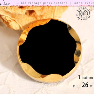 Puede incluir: Un botón de cristal vintage redondo con un centro negro sólido rodeado por un borde metálico dorado reflectante con un borde ondulado. El botón tiene un diámetro de aproximadamente 26 mm. El texto en la imagen incluye "rosa day", "old vintage glass buttons", "anno 1940/50/60", "design by karin" y "1 button ø ca 26 mm".