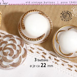 May include: Three vintage white buttons with gold-colored decorative accents. The buttons are approximately 22 mm in diameter. The image includes text that reads "old vintage buttons" and "anno 1940/50/60".