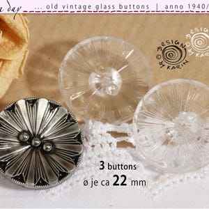 Peut inclure: Trois boutons circulaires, dont un bouton en métal argenté avec un motif de pétales radiaux et deux boutons en verre transparent avec un design similaire en rayons de soleil. Chaque bouton mesure environ 22 mm de diamètre selon le texte.