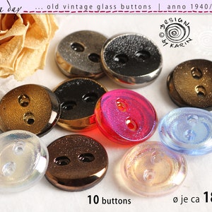Może przedstawiać: Dziesięć vintage szklanych guzików w różnych kolorach i wykończeniach, w tym tęczowe, przezroczyste, złote, czarne i czerwone. Guziki są dwu-otworowe i mają średnicę około 18 mm. Tekst "Ø je ca 18 mm" i "10 buttons" jest widoczny na zdjęciu.