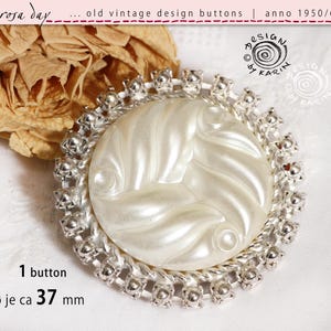 Peut inclure: Bouton de design vintage des années 1950/60. Le bouton a un centre nacré avec un motif tourbillonnant, entouré d'un cadre argenté orné. Le bouton mesure environ 37 mm de diamètre.