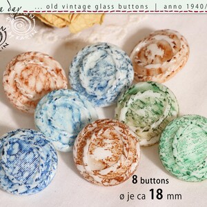 Może przedstawiać: Osiem zabytkowych szklanych guzików w odcieniach niebieskiego, brązowego i zielonego. Każdy guzik ma unikalny marmurkowy wzór i średnicę około 1,8 cm. Guziki pochodzą z lat 40., 50. i 60.