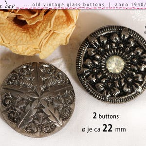 Op de afbeelding: Twee antieke zilverkleurige glazen knopen. Eén knoop heeft een sterpatroon, de andere een bloemmotief met een centrale edelsteen. De knopen hebben een diameter van ongeveer 22 mm. De afbeelding bevat de tekst "old vintage glass buttons | anno 1940/50/60".
