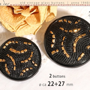 Può includere: Due bottoni vintage neri in vetro con dettagli color oro. I bottoni hanno una superficie strutturata e misurano circa 22-27 mm di diametro. Il testo dell'immagine dice "old vintage glass buttons" e "anno 1940/50/60".