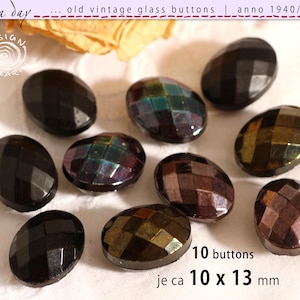 Pode incluir: Um conjunto de dez botões de vidro ovais com superfície facetada. Os botões apresentam tons escuros e iridescentes de preto, bronze e verde profundo. O texto indica 10 botões, cada um medindo aproximadamente 10 x 13 mm.