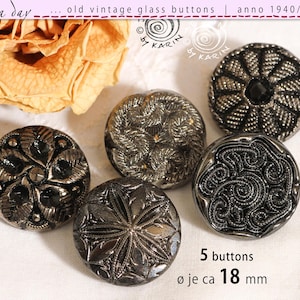 Könnte beinhalten: Fünf runde Vintage-Glasknöpfe mit detaillierten dunkelgrauen Metallic-Reliefmustern. Jeder Knopf weist ein einzigartiges geprägtes Design auf, darunter florale, geometrische und geschwungene Motive. Der Text gibt 5 Knöpfe mit einem Durchmesser von ca. 18 mm an.