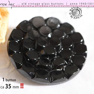 Könnte beinhalten: Ein schwarzer Vintage-Glas-Knopf mit einem strukturierten, kreisförmigen Design. Der Knopf hat eine Reihe von erhabenen, abgerundeten Formen auf seiner Oberfläche. Der Text "rosa day" und "old vintage glass buttons" ist sichtbar. Der Knopf hat einen Durchmesser von ca. 3,5 cm.