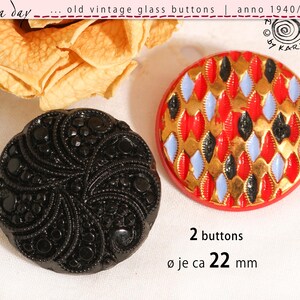 May include: Two round glass buttons measuring 22 mm in diameter. One button is solid black with a swirling, beaded texture. The second button features a red base with a repeating diamond pattern in gold, black, and light blue colours.