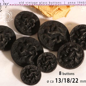 Può includere: Una collezione di otto bottoni antichi in vetro nero con un motivo floreale in rilievo. I bottoni hanno diametri di circa 13, 18 e 22 mm. L'immagine include il testo "old vintage glass buttons" e "8 buttons".