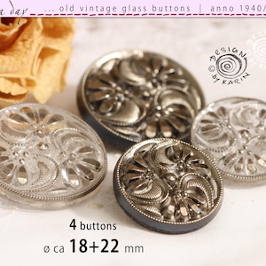 Könnte beinhalten: Ein Set aus vier runden Glasknöpfen mit erhabenem Blumen- und Schnörkelmuster. Die Knöpfe sind klar und metallisch grau, zwei messen 18 mm und zwei 22 mm im Durchmesser. Der Text 4 buttons und 18+22 mm ist deutlich zu sehen.