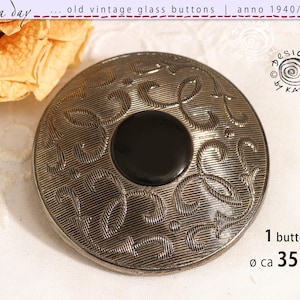 May include: A round button with a metallic silver finish featuring an intricate embossed pattern of swirling lines and a smooth black circular centre. The button has a diameter of approximately 35 mm as indicated by the text on the image.