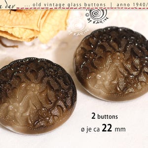 Op de afbeelding: Twee vintage bruine glazen knopen met gedetailleerde bloemmotieven. De ronde knopen hebben een diameter van ongeveer 22 mm. De afbeelding bevat de tekst "old vintage glass buttons" en "anno 1940/50/60".