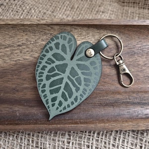 May include: A green leather keychain shaped like a leaf with a metal ring and clasp. The keychain has the initials "CM" embossed on it.