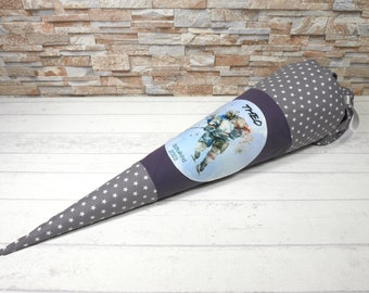 May include: A gray and white fabric cone with a blue and white illustration of a hockey player. The cone has a purple band with the text "Theo" and "Schuleinführung 2023" printed on it.