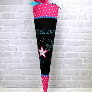 May include: A pink and black school cone with white stars and a blue ribbon. The cone has the name "Isabella" embroidered on it.