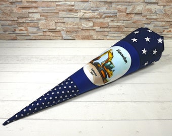 May include: A blue and white school cone with white stars. The cone has a circular patch with a yellow excavator and the text "Maximilian September 2023".