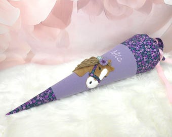 May include: A cone-shaped fabric gift bag in lavender, featuring a floral pattern at the top and bottom. The center displays an embroidered brown horse head with a yarn mane and a purple flower accessory. The name Mia is embroidered in white script.
