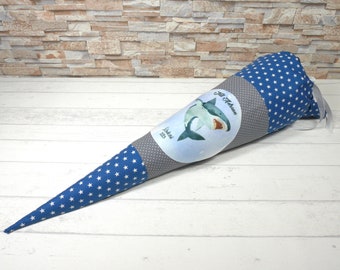 May include: A blue and gray school cone with white stars and a shark graphic. The cone has the text "Lil' Atara" and "Schule 2023" on it.