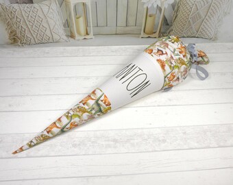 May include: A white and brown school cone with a grey ribbon. The cone is decorated with a pattern of animals and the name "Anton" is written on the side.