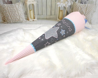 May include: A pink and gray school cone with a blue ribbon and silver glitter stars. The cone has the name "Melina" embroidered on it.