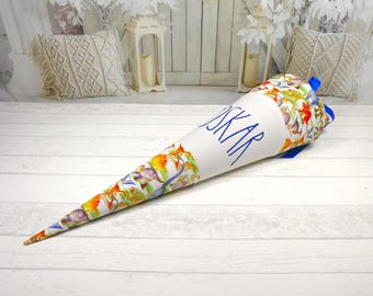 May include: A white and blue school cone with a dinosaur print and the name "Oskar" embroidered in blue.
