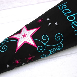 May include: Black school bag with a large pink and white star, blue swirls, and silver stars. The bag is personalized with the name "Isabella".