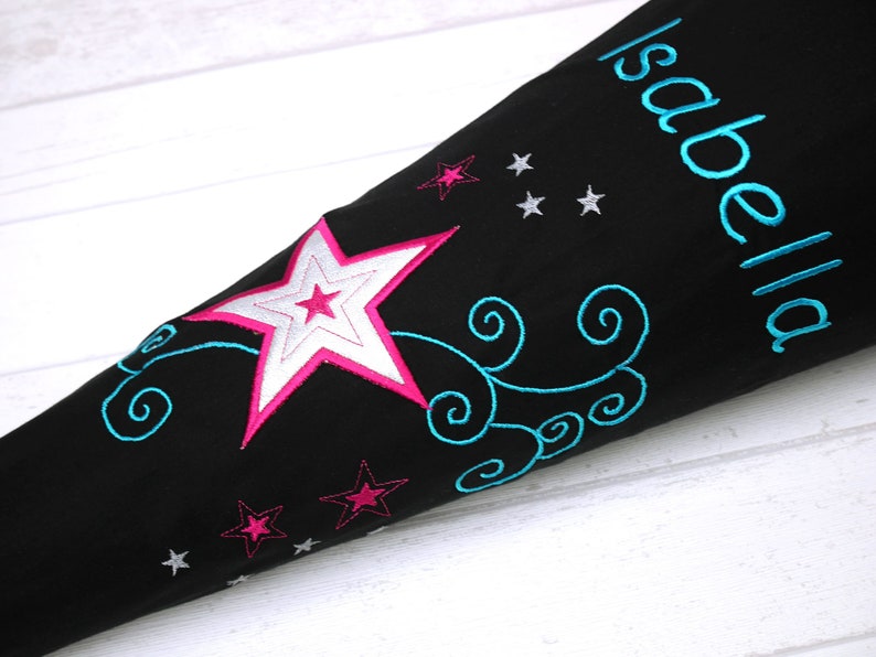 May include: Black school bag with a large pink and white star, blue swirls, and silver stars. The bag is personalized with the name "Isabella".