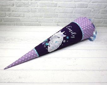 May include: A conical school cone featuring a dark purple fabric body with an embroidered white unicorn and the name Emily. The top and bottom sections are made of light purple fabric with a white star pattern, accented by light blue ribbon ties.