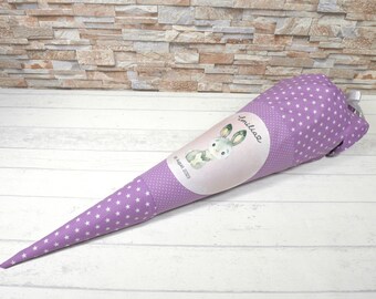 May include: A purple fabric cone with white stars and a bunny rabbit design. The cone has the name "Emilia" and the date "8. April 2023" printed on it.