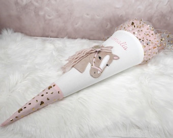 May include: A conical school cone featuring a white textured body with a beige horse applique, pink yarn mane, and the name Amalia in script. The base is light pink with gold hearts, and the top is finished with sheer pink tulle and gold hearts.
