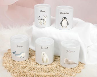 May include: Five white ceramic piggy banks with animal illustrations and personalized names. The names are Clara, Matilda, Emma, Samuel, and Johanna. The animals are a snow leopard, penguin, narwhal, polar bear, and seal.