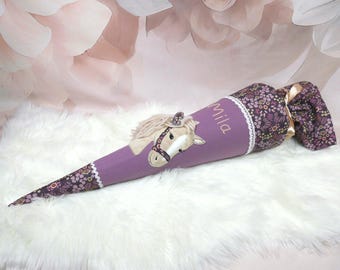 May include: A cone-shaped school gift bag featuring a light purple fabric body with a beige horse applique, white lace trim, and a dark purple floral patterned fabric top. The name Mila is embroidered in white script on the purple section.