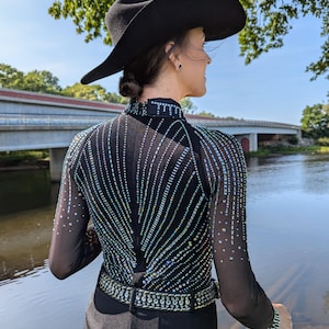 May include: A black long-sleeved shirt with a sequined design and a black belt. The shirt is worn by a person wearing a black cowboy hat. The person is standing in front of a body of water.