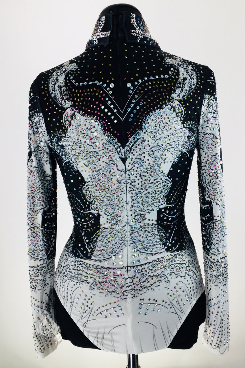 May include: A black and white long-sleeved shirt with a rhinestone design. The shirt has a high neck and a fitted silhouette.