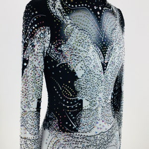 May include: A black and white long-sleeved shirt with a rhinestone design. The shirt has a high collar and a fitted silhouette.