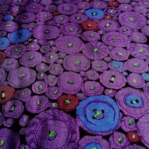 Könnte beinhalten: Lilafarbener Stoff mit einem sich wiederholenden Muster aus blauen, grünen und roten Kreisen. Die Kreise haben ein Knopf-ähnliches Design.