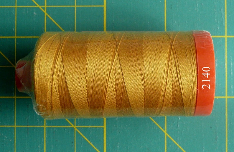 K&ouml;nnte beinhalten: Eine Spule goldfarbenen Garns mit einem roten Etikett mit der Aufschrift "2140".