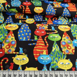 Könnte beinhalten: Ein schwarzer Stoff mit einem sich wiederholenden Muster aus stilisierten Katzen in verschiedenen Farben wie Gelb, Rot, Blau und Grün mit geometrischen Formen und Sternmotiven. Ein weißes Maßband liegt unten und zeigt 36 cm an.