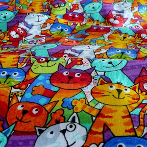 Könnte beinhalten: Ein farbenfroher Stoff mit einem sich wiederholenden Muster von Cartoon-Katzen. Die Katzen sind in verschiedenen Farben dargestellt, darunter Orange, Rot, Blau und Grün, mit weißen Akzenten. Der Hintergrund hat lila und Regenbogenstreifen.