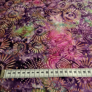 Könnte beinhalten: Lilafarbener Stoff mit einem sich wiederholenden Muster aus goldenen Kreisen und Sternen. Ein weißes Maßband liegt auf dem Stoff und zeigt Maße von 2 bis 22 Zoll.